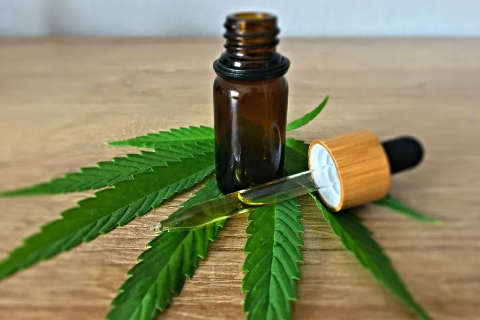 Folha de cannabis com frasco aberto de óleo de cannabis